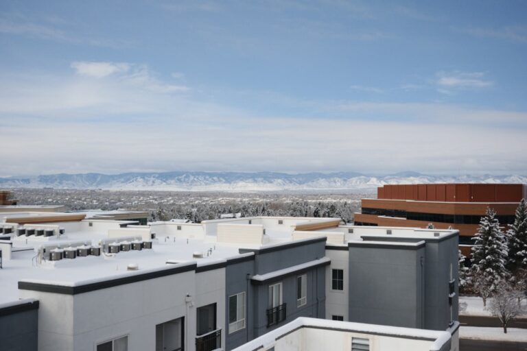 A person in workwear inspects a flat, snow-dusted commercial roof next to HVAC units and cleared roof drains.