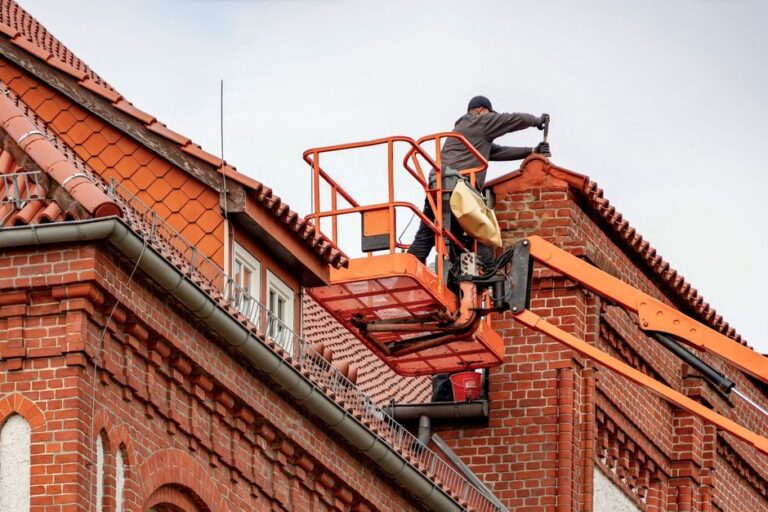 A maintenance worker inspecting a flat commercial roof with visible stains and debris under cloudy skies.